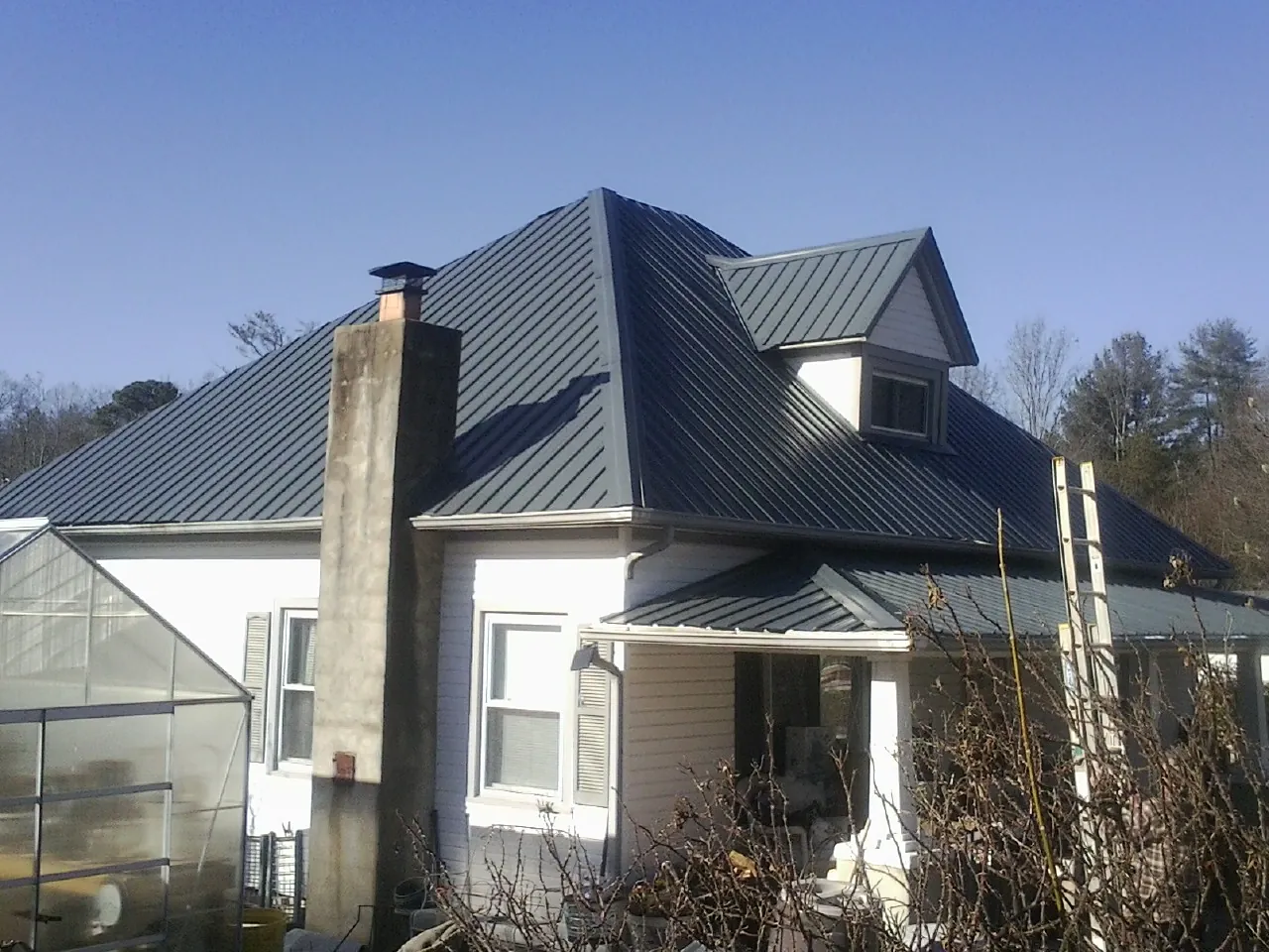 Dark blue standing seam metal roof on a white farmhouse with dormer — Slate & Tile Roof Repair by Roofing Brothers in Central Valley
