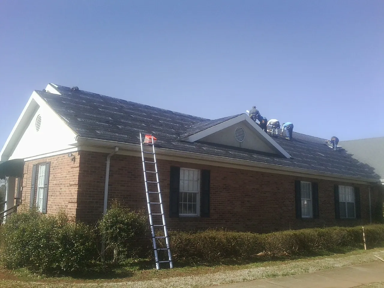 Crew tearing shingles off a brick ranch roof with a ladder set — Emergency Roof Repair work by our crew in Central Valley