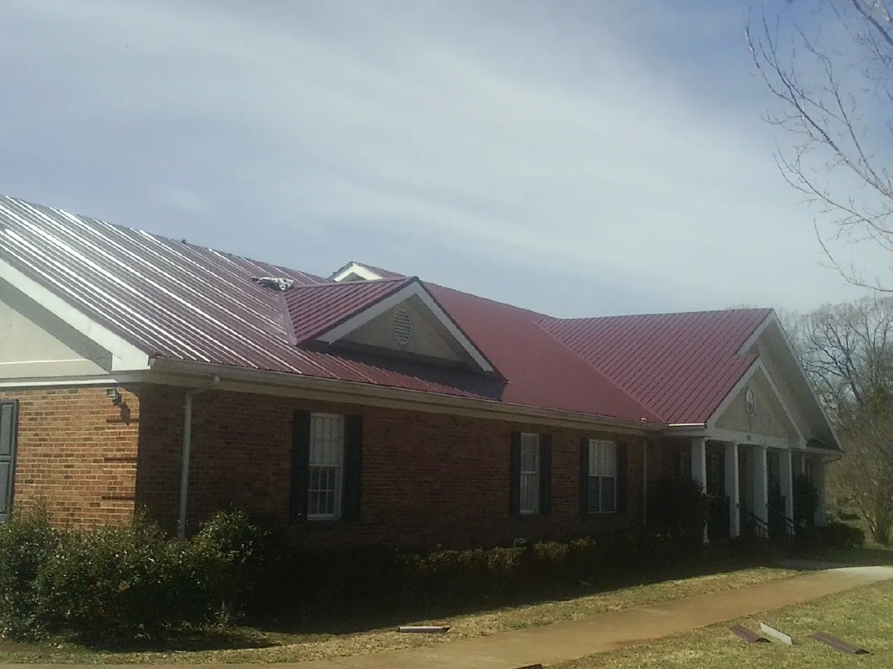 Red metal roof with gabled entries on a long brick building, from a Hail Damage Roof Repair job in Central Valley