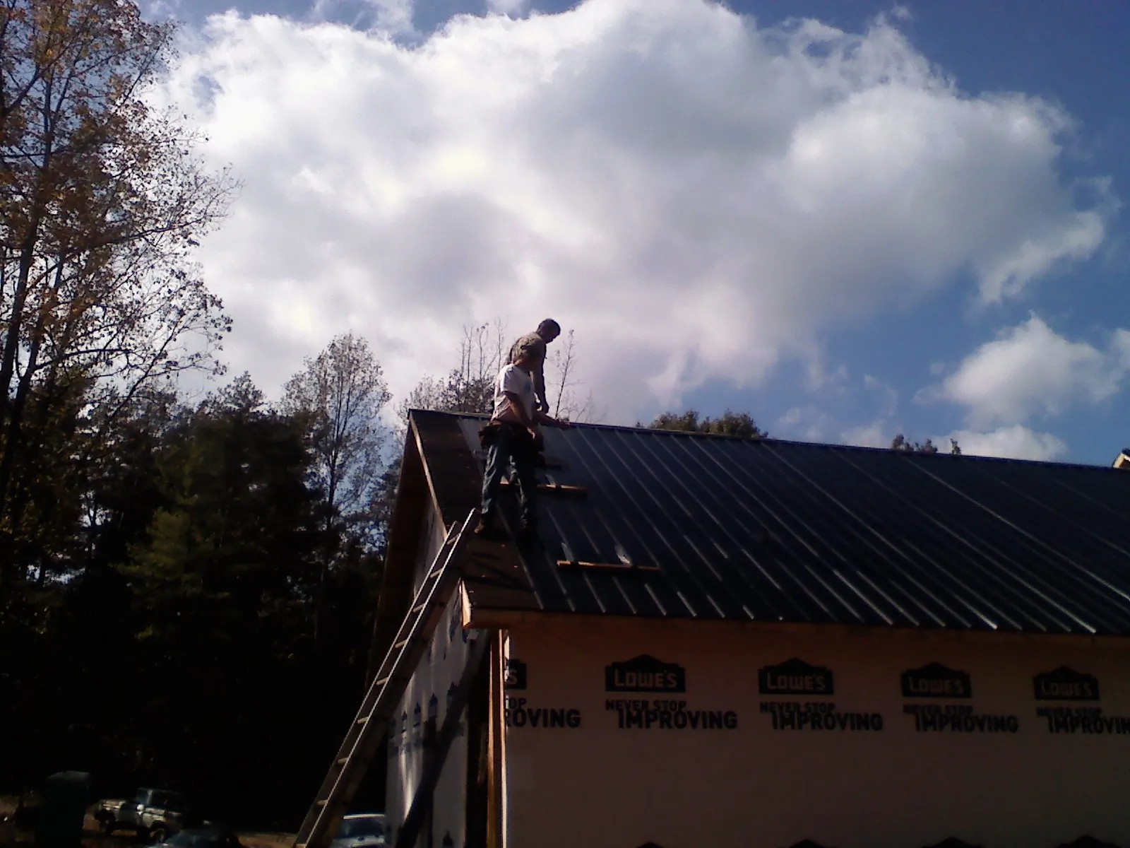 Roofer fastening dark metal panels high against a cloudy sky, from a Roof Inspection job in Central Valley