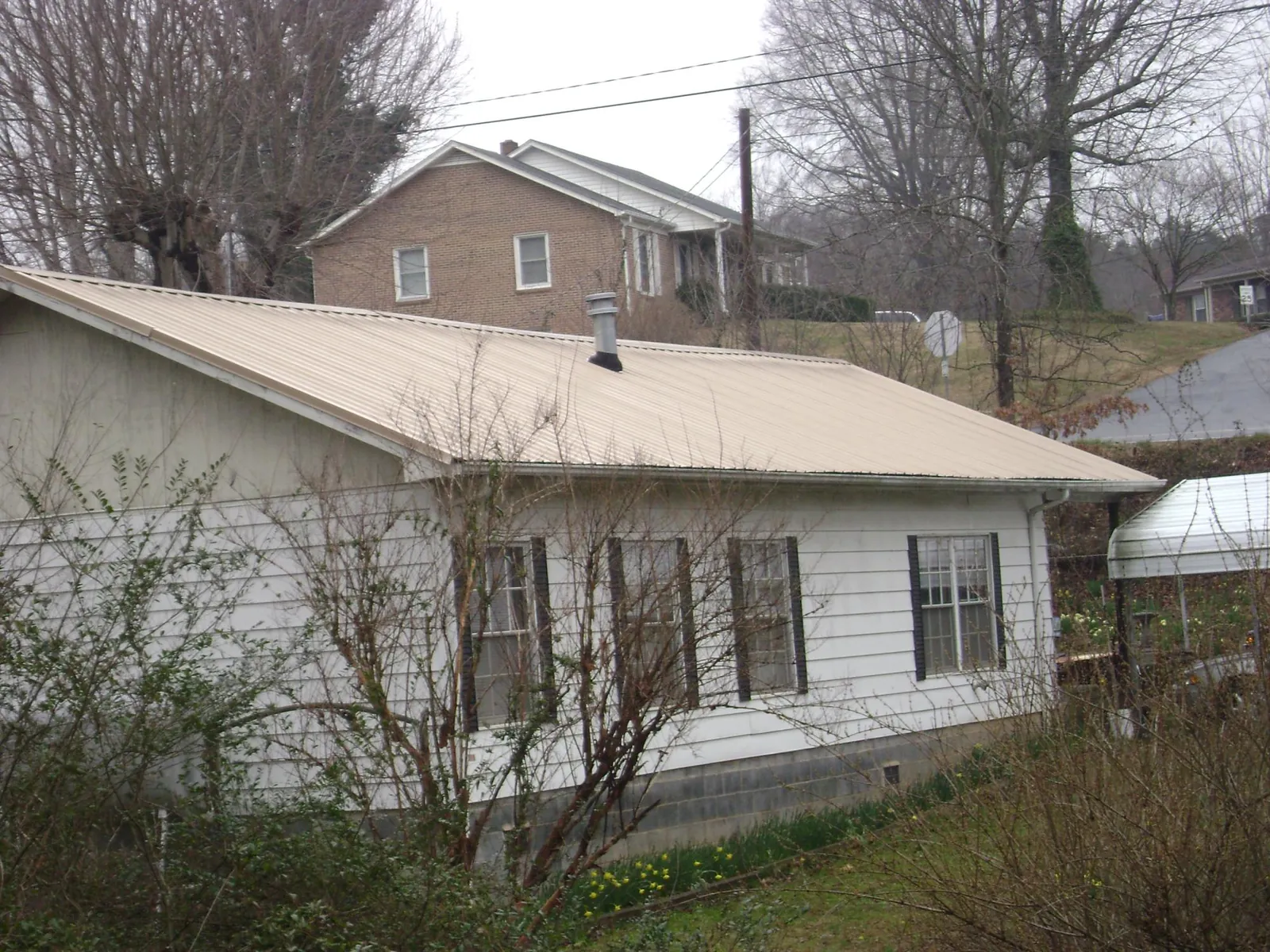 Tan metal roof on a white sided house set into a hillside — Commercial Roofing by Roofing Brothers in Central Valley